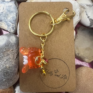 May include: A gold-coloured keyring with a lobster-shaped charm. The charm is orange and translucent with white eyes. The keyring is attached to a brown tag with the text "Holly and Lili" in a circle.