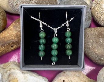 Puede incluir: Un conjunto de pendientes y un collar de cuentas de piedra verde con cadena y ganchos de plata. Las joyas se muestran en una caja de terciopelo negro.