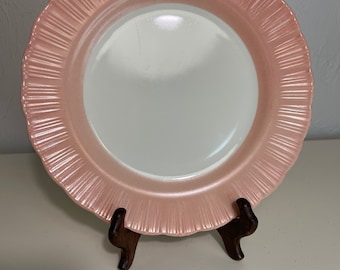 Może przedstawiać: Różowy ceramiczny talerz z falistym brzegiem i białym środkiem. Talerz stoi na drewnianym stojaku.