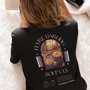 May include: Black t-shirt with a graphic print of a window scene with bowls of soup. The text "FEYRE DARLING SOUP CO." is printed on the shirt.
