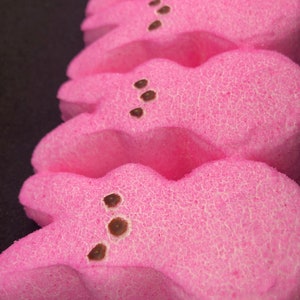 May include: A stack of pink marshmallow Peeps, a popular Easter treat, with chocolate chips for eyes.