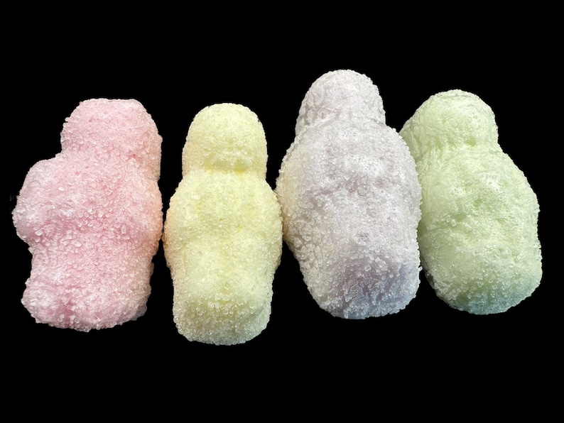 May include: Four sugar-coated marshmallow candies in the shape of people. The candies are pink, yellow, purple, and green.