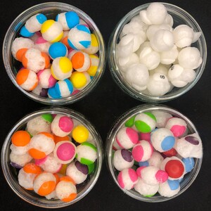 May include: Four glass jars filled with colorful candy. The jars are arranged in a square pattern on a black surface. The candy is a mix of white, red, blue, green, yellow, and orange.