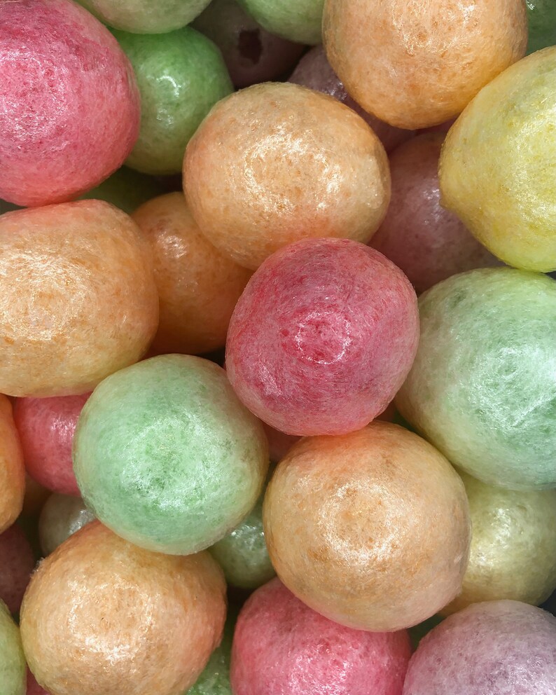 May include: A close-up of a pile of colorful, round, textured, bubble wrap packing peanuts. The peanuts are in shades of pink, orange, green, and yellow.