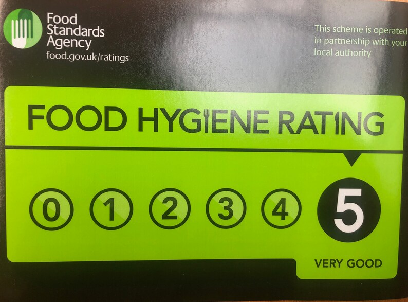 May include: A green and black food hygiene rating sticker with a white number 5 in a black circle. The text "VERY GOOD" is below the number. The sticker is from the Food Standards Agency and includes the website food.gov.uk/ratings.