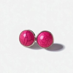 May include: A pair of round stud earrings with a bright pink, cracked stone design set in a silver-colored metal. The earrings are displayed on a white background, showcasing their vibrant color and texture.