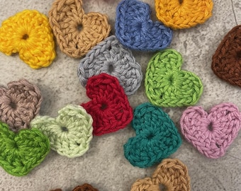 Puede incluir: Una colección de 15 corazones tejidos a crochet en varios colores, incluyendo rosa, amarillo, azul, gris, rojo, verde, marrón y morado.