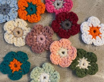 May include: Ten crocheted flower shapes in various colors, including teal, orange, pink, white, red, and green. The flowers are all the same size and shape, with five petals and a center circle.