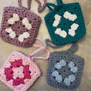 May include: Four crocheted soap savers with different colored squares and white accents. Each soap saver has a loop for hanging.