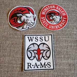 May include: Three embroidered patches featuring the Winston-Salem State University logo. The logo is a red ram's head with white horns and a white face. The patches are white with black outlines and the words "WSSU" and "R.A.M.S." in black.