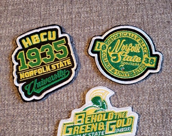 Może przedstawiać: Trzy haftowane naszywki z logo Uniwersytetu Stanowego Norfolk. Pierwsza naszywka jest zielona i czarna z tekstem "HBCU 1935 NORFOLK STATE University". Druga naszywka jest zielona i czarna z tekstem "Historically Black College & University Norfolk State Spartans 1935". Trzecia naszywka jest zielona i złota z tekstem "Behold the Green & Gold Norfolk State Spartans".