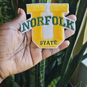 May include: A white felt patch with a yellow embroidered "U" and the text "NORFOLK STATE" in green embroidery.