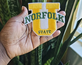 May include: A white felt patch with a yellow embroidered "U" and the text "NORFOLK STATE" in green embroidery.