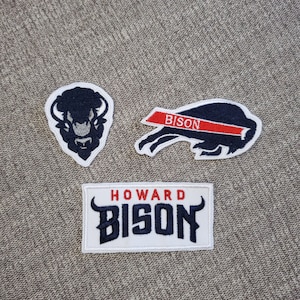 May include: Three embroidered patches featuring a black and white bison head, a black and white bison running with a red ribbon that says "BISON", and a white patch with the text "HOWARD BISON" in black.