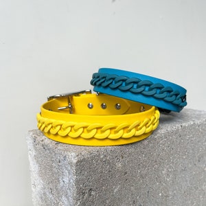 Könnte beinhalten: Zwei Hundehalsbänder, eines gelb und eines blaugrün, mit einem Kettenglied-Design. Die Halsbänder sind aus einem weichen, flexiblen Material.