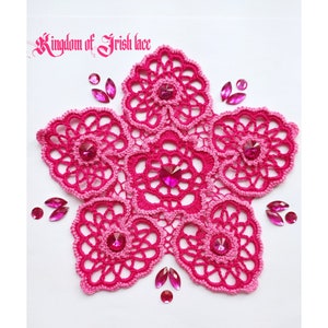 Op de afbeelding: Een handgemaakt, stervormig kleedje in roze tinten, versierd met sprankelende roze strass-steentjes. Het kleedje is gemaakt van delicate Ierse kant en bevat de tekst "Kingdom of Irish lace".