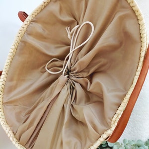 May include: A round, woven basket with a beige fabric liner and a drawstring closure. The basket is made of natural materials and has a light brown color.
