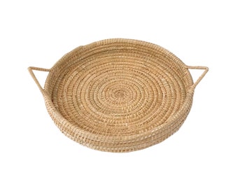 May include: A round woven tray with two handles. The tray is made of natural materials and has a light brown color.