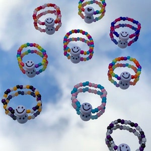 Op de afbeelding: Tien kleurrijke kralenringen met smiley-bedels. Elke ring is gemaakt van twee strengen kleurrijke kralen.
