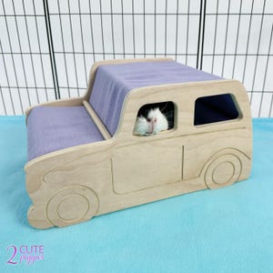 May include: A wooden car-shaped guinea pig hideaway with a purple fleece lining. The hideaway has a window opening and a guinea pig is peeking out of the window.