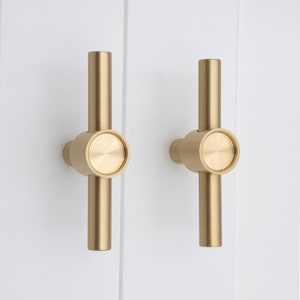 Peut inclure: Deux poignées de porte de placard en forme de T de couleur or. Les poignées ont un bouton rond à l'intersection du T.