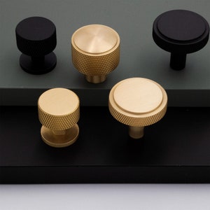 May include: Five cabinet knobs, two black and three gold. The gold knobs have a textured, ridged design. The black knobs have a smooth, round design.