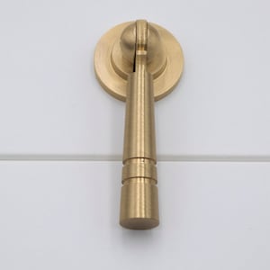 May include: A gold-toned cabinet pull with a round knob and a cylindrical handle.