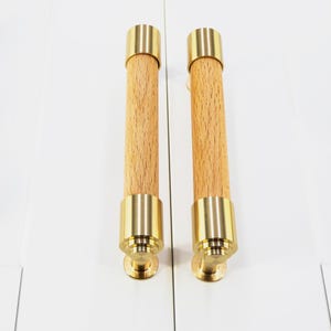 May include: Two gold and wood cabinet pulls with a cylindrical shape. The pulls have a brass finish and a wood centre.