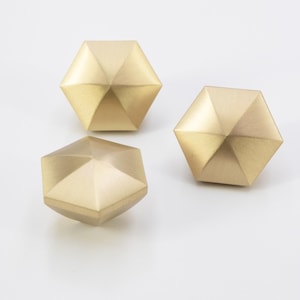 May include: Three gold-toned, geometric cabinet knobs with a hexagonal shape and a faceted design.