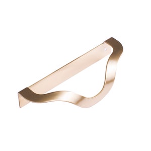 May include: A gold-colored metal cabinet pull with a wavy design. The pull is about 10 inches long.