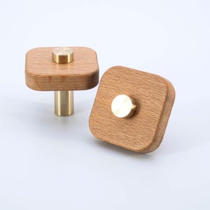 May include: Two square wooden knobs with brass accents. The knobs have a rounded top and a cylindrical base.