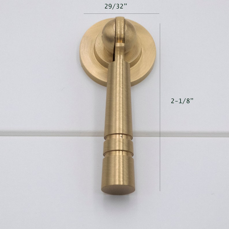 K&ouml;nnte beinhalten: Ein goldfarbener Schrankgriff mit runder Basis und einem zylindrischen Griff. Der Griff ist 5,4 cm hoch und 2,3 cm breit.