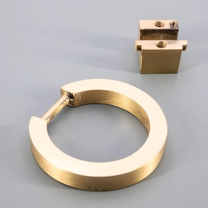 K&ouml;nnte beinhalten: Ein goldfarbener, runder Ring-Griff aus Metall mit glatter Oberfl&auml;che. Der Griff ist f&uuml;r Schr&auml;nke oder Schubladen konzipiert.