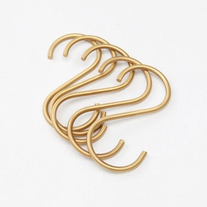 May include: A set of six gold-toned S-shaped hooks. The hooks are made of metal and have a smooth, polished finish.