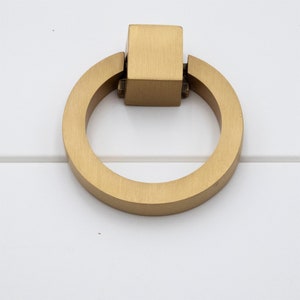 K&ouml;nnte beinhalten: Ein goldener Ring-Kabinettgriff mit quadratischer Oberseite.