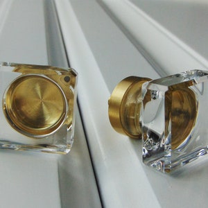 May include: Two square clear glass cabinet knobs with a brass centre. The knobs have a bevelled edge and a smooth, polished finish.