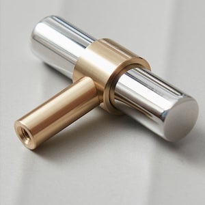 Peut inclure: Une poignée de porte en forme de T avec une finition chromée polie et un accent en laiton. La poignée a une forme ronde et une surface lisse.