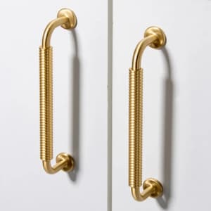May include: Two gold-toned cabinet pulls with a ribbed design. The pulls are L-shaped with a rounded top and bottom.