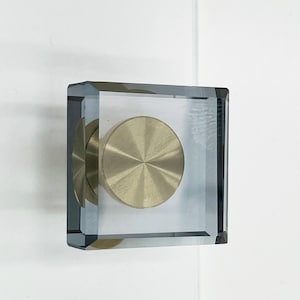 May include: A square clear glass cabinet knob with a brushed gold round knob inside.