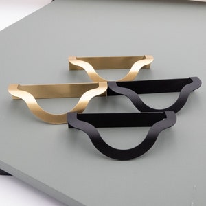 May include: Three cabinet pulls in a wavy design. Two are gold and one is black.