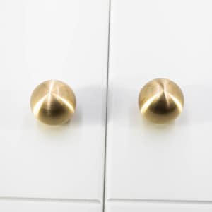 May include: Two round, brushed gold cabinet knobs. The knobs are smooth and have a shiny finish.