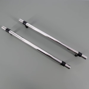 May include: Two shiny, chrome-finished cabinet handles with black rubber grips. The handles are straight, cylindrical, and appear to be made of metal. They are set against a plain, gray background.