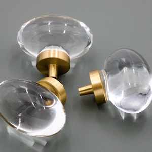 May include: Three clear glass cabinet knobs with gold metal bases. The knobs are round and oval shaped.