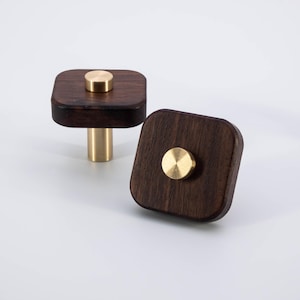 May include: Two square wooden cabinet knobs with a brass finish. The knobs have a square base and a round brass knob on top.