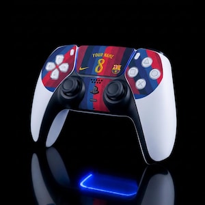 Op de afbeelding: Een wit en zwart draadloze gamecontroller met een aangepaste skin met rode en blauwe verticale strepen, de tekst YOUR NAME, het cijfer 8, een Nike-logo en het FC Barcelona-embleem op het centrale touchpad tegen een zwarte achtergrond.
