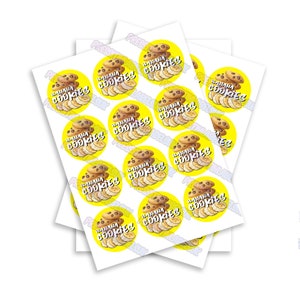Könnte beinhalten: Ein Stapel weißer Papierbögen mit aufgedruckten gelben Kreisen. Jeder Kreis zeigt einen Stapel Schokoladenkekse mit Bananenscheiben auf gelbem Hintergrund. Der Text "BANANA COOKIES" ist in Weiß auf jedem Kreis geschrieben.