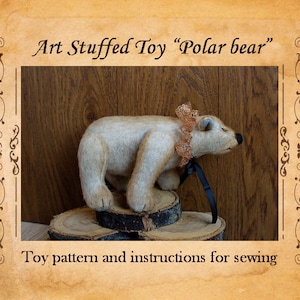 Pode incluir: Um urso polar de pelúcia feito à mão, em pé sobre uma base de madeira. O urso é branco sujo com um nariz preto e uma gola decorativa. A imagem inclui o texto "Art Stuffed Toy 'Polar bear'" e "Toy pattern and instructions for sewing."