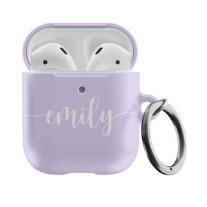 May include: A lilac-colored AirPods case with the name "emily" in a cursive font. The case is open, revealing white earbuds. A silver carabiner clip is attached to the side for easy carrying.