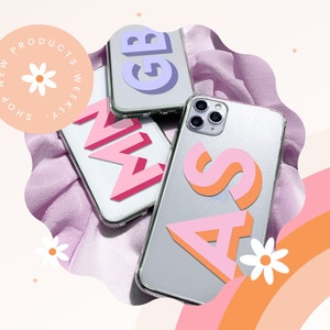 May include: Clear phone cases with colourful 3D letter designs. The letters are pink, orange, and purple. The image also includes the text "NEW PRODUCTS WEEKLY SHOP". The background has a pink and orange rainbow.