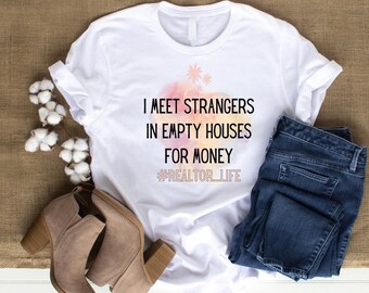 Può includere: Maglietta bianca con uno sfondo ad acquerello e il testo "I meet strangers in empty houses for money #realtor_life". La maglietta è abbinata a jeans blu e stivaletti marroni.